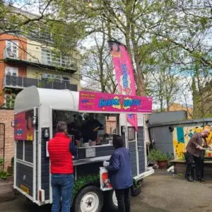 The Bubble Waffle Bar horsebox set up in an urban courtyard with people placing orders.