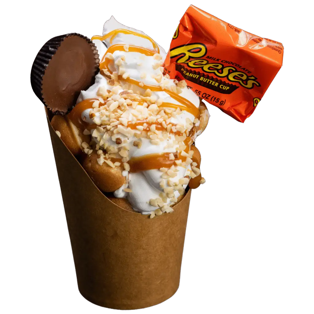 Bubble waffle with whipped cream, crushed nuts, caramel drizzle, and Reese's peanut butter cup and wrapper.