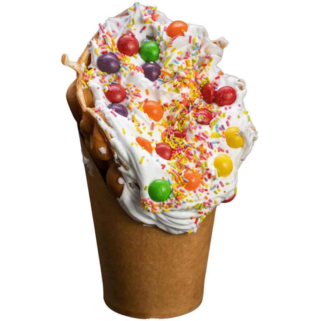 Bubble waffle with whipped cream, rainbow sprinkles, and colourful Skittles candy on top.