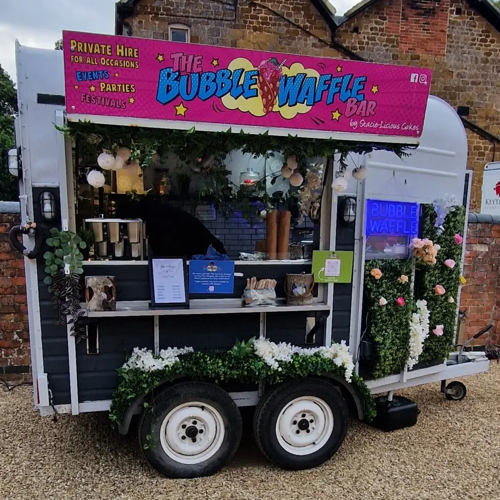 A decorated vintage horsebox serving as The Bubble Waffle Bar, adorned with flowers and greenery, ready for service.