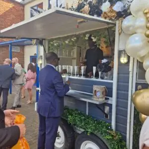 A man in a suit being served a drink from the decorated Bubble Waffle Bar setup at an outdoor event.