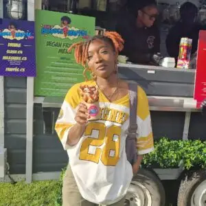 A woman stands in front of the vegan-friendly menu holding a bubble waffle and looking confidently at the camera.