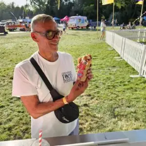 A man in sunglasses smiles while holding a bubble waffle at an outdoor food festival.