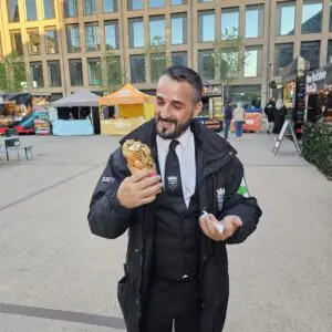 A security guard smiles while holding a bubble waffle at an outdoor street food market.